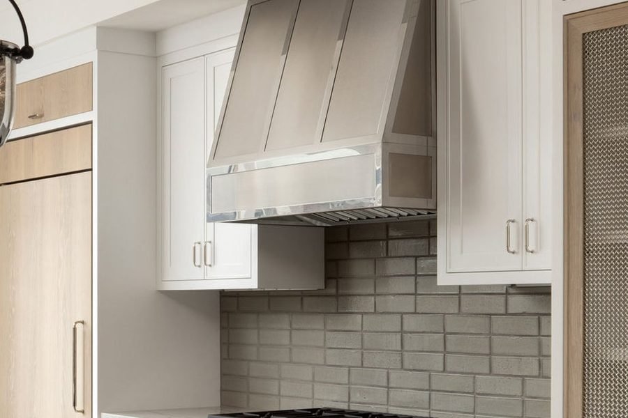 Stainless steel range hood above a professional range in a white kitchen